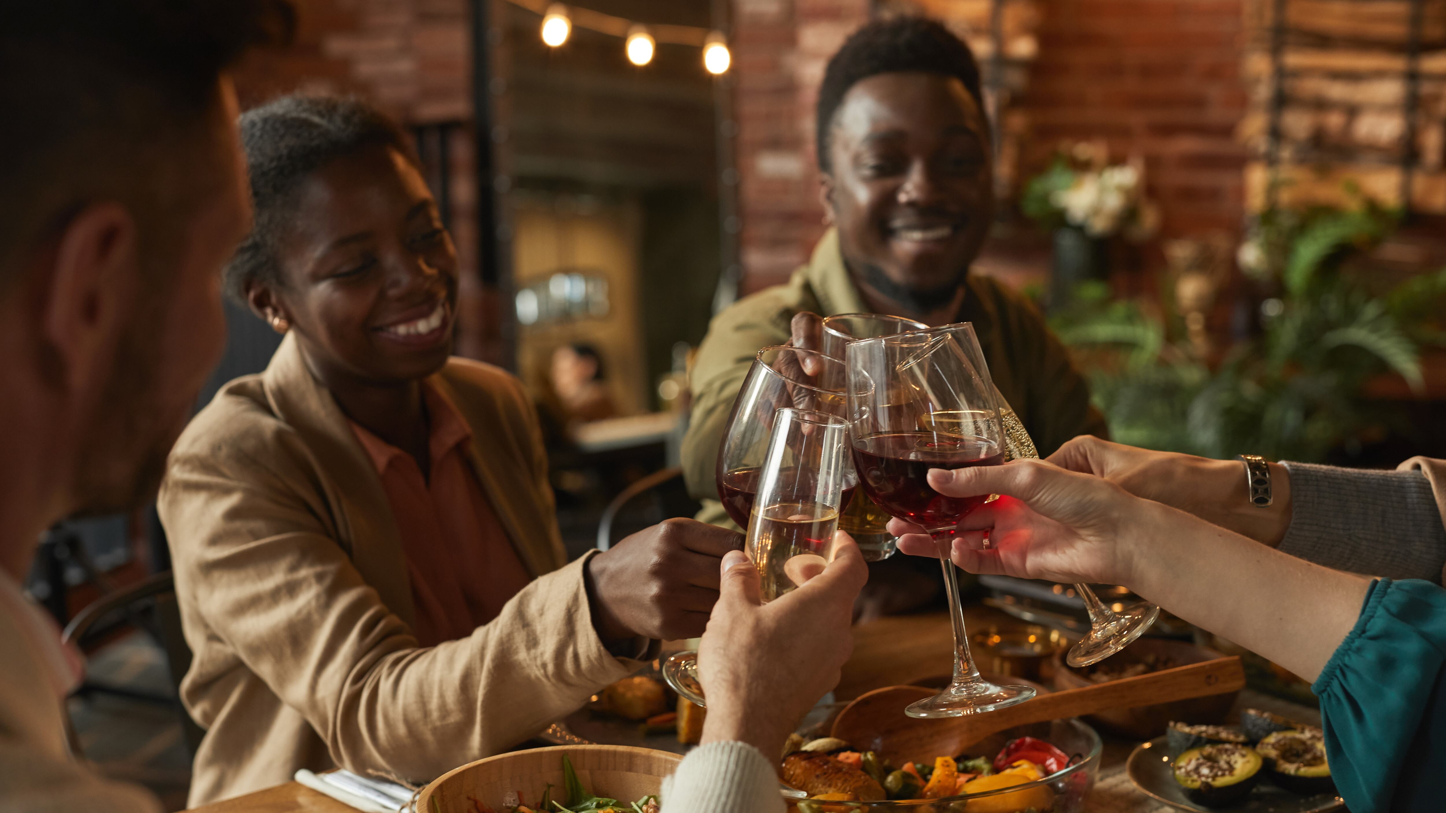 Portrait of happy couple clinking glasses while enjoying dinner party with friends and family in cozy interior