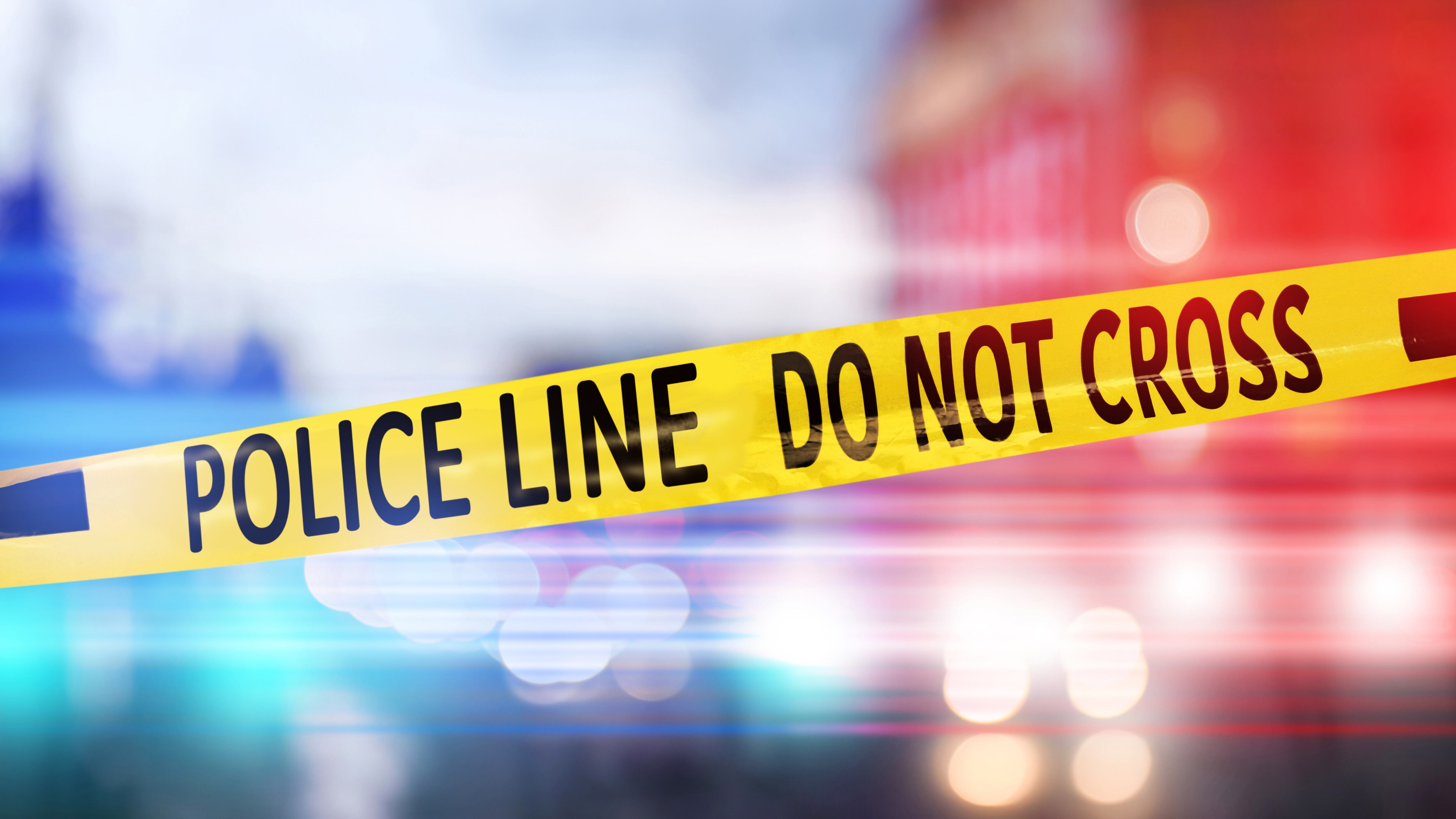 Yellow law enforcement tape isolating crime scene. Blurred view of city, toned in red and blue police car lights